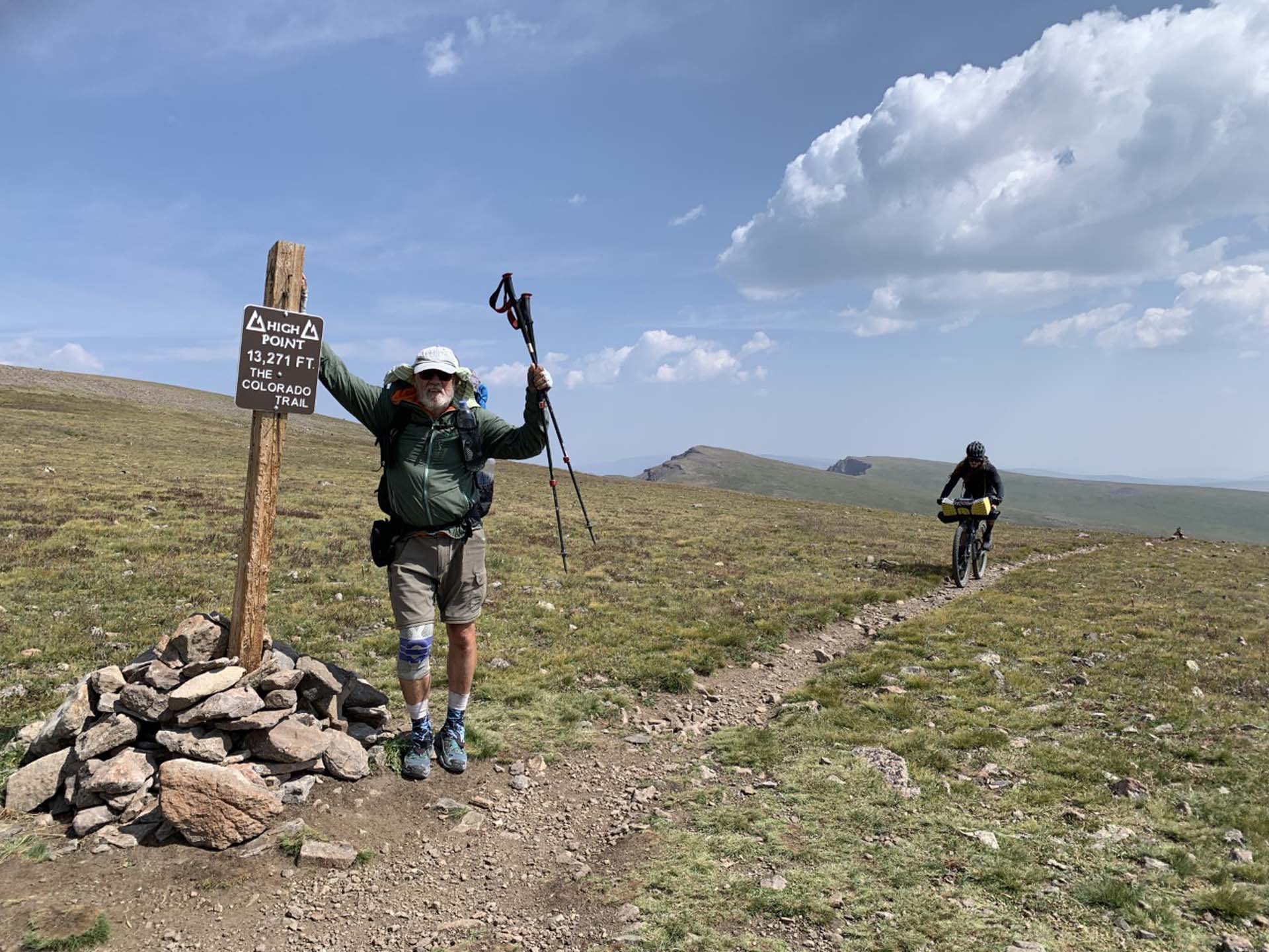 man celebrates reaching high point with biker riding up trail